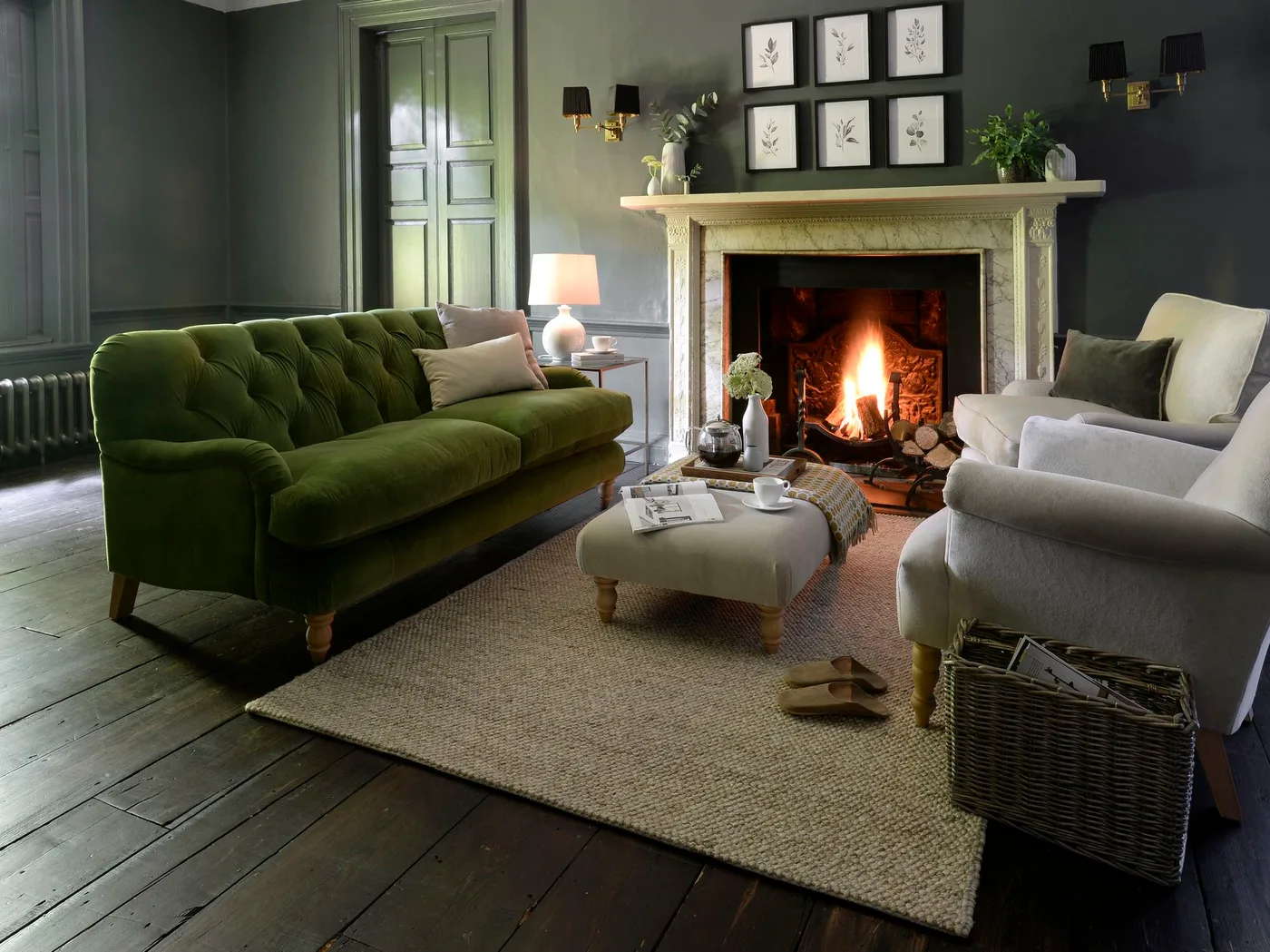 Light fireplace surround against dark gray walls with botanical picture group, green sofa, pale armchair and plain rug.