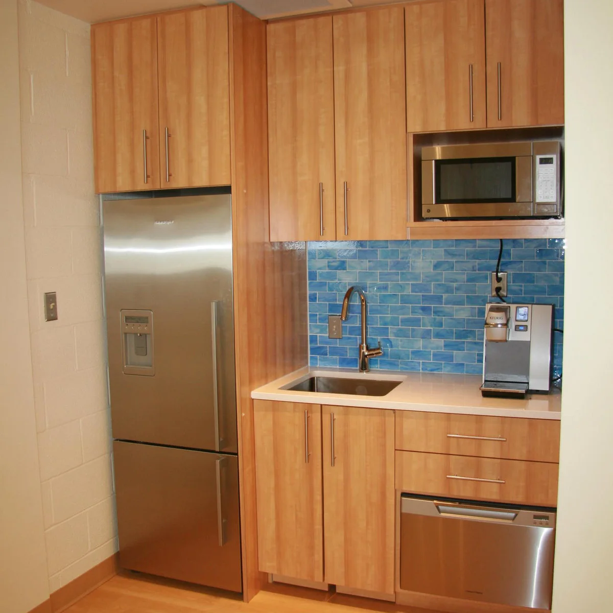 Wood-cabinet kitchenette with a tall stainless refrigerator, blue tile and an upper microwave