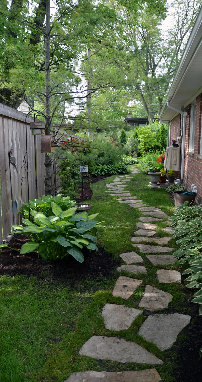 Irregular pale stepping stones wind through grass between a timber fence and a brick house