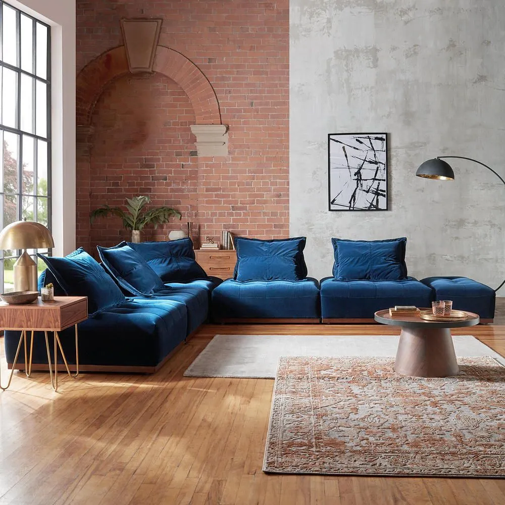 A blue sectional sits against exposed brick beside pale walls and timber floors.
