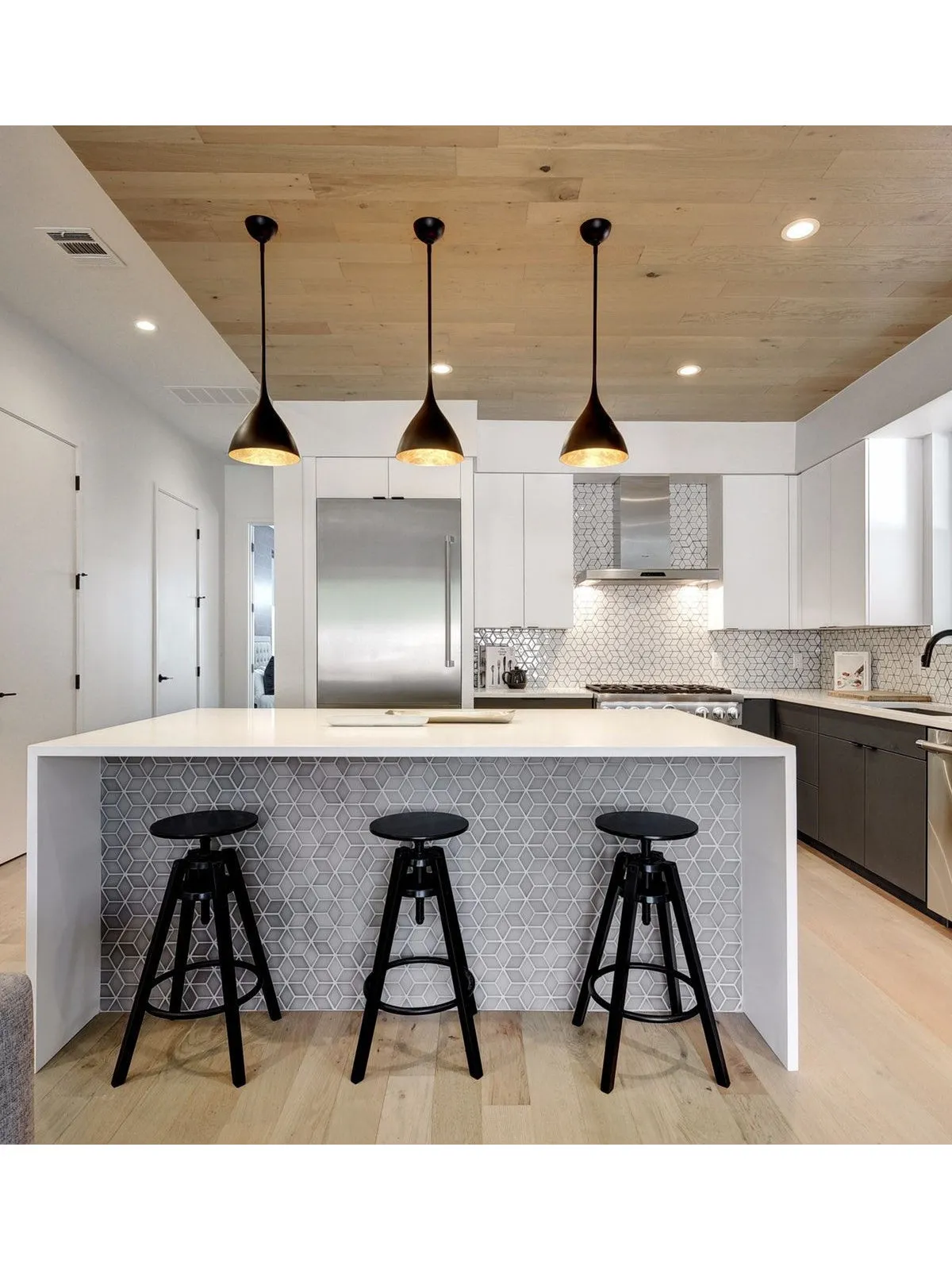 Dark lower cabinets line a bright kitchen beside a pale island and black stools.
