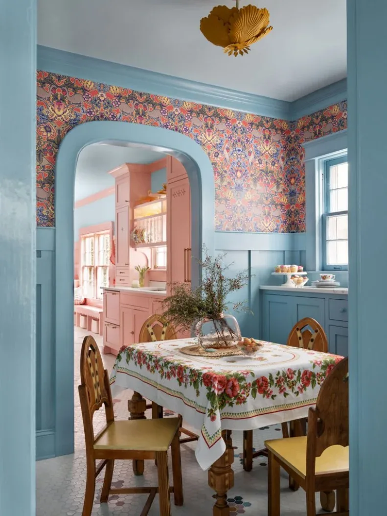 Pale blue dining wall paneling and arched doorway trim beneath colorful patterned wallpaper beside a small table