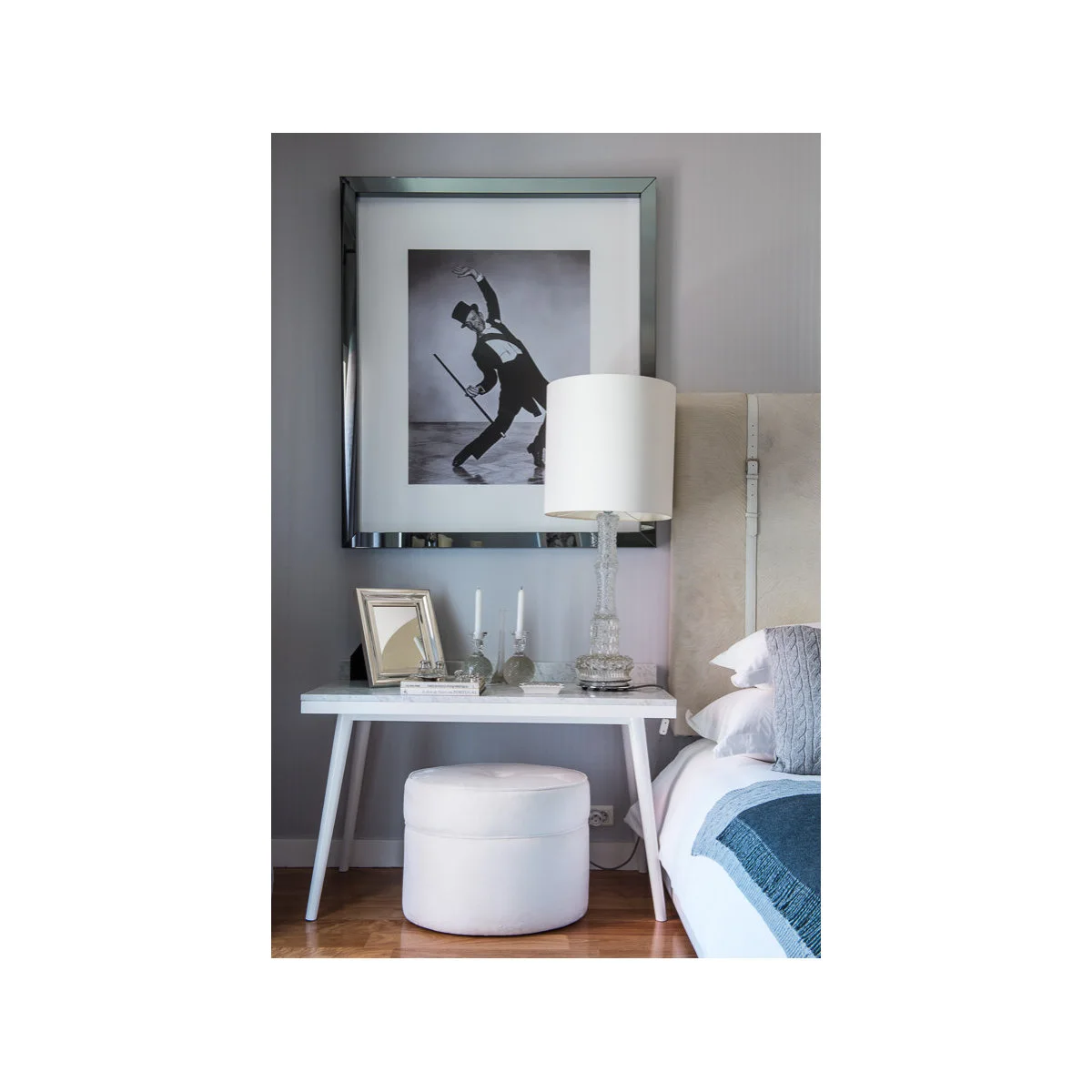 A compact white table with a small framed mirror and round stool sits beside a bed