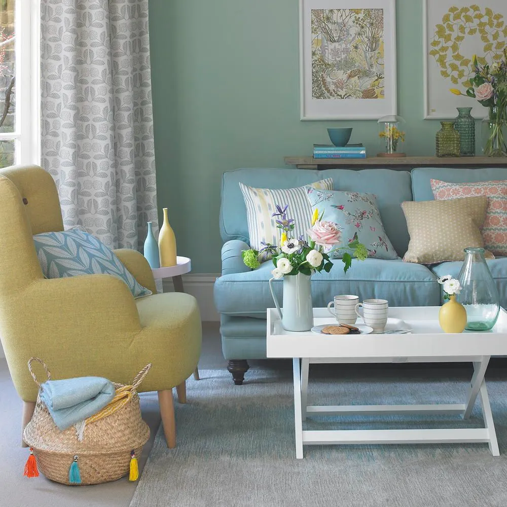A pale blue sofa shares a softly colored room with a yellow armchair and light table.