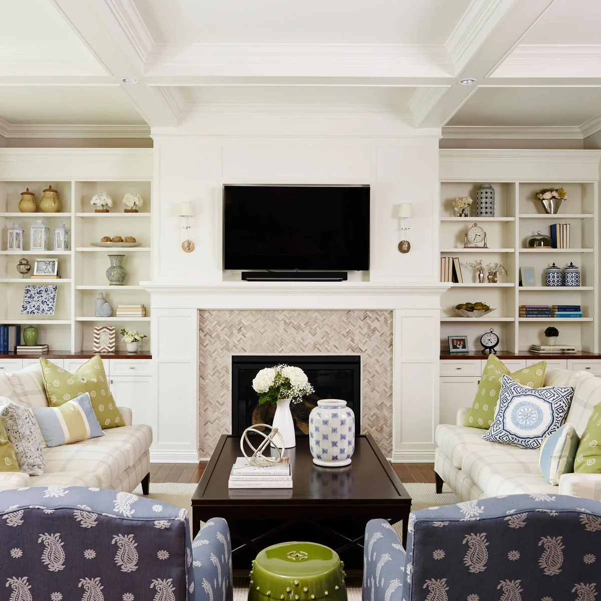 Pale sofas face each other beside a fireplace and television, with two blue patterned chairs closing the near end.