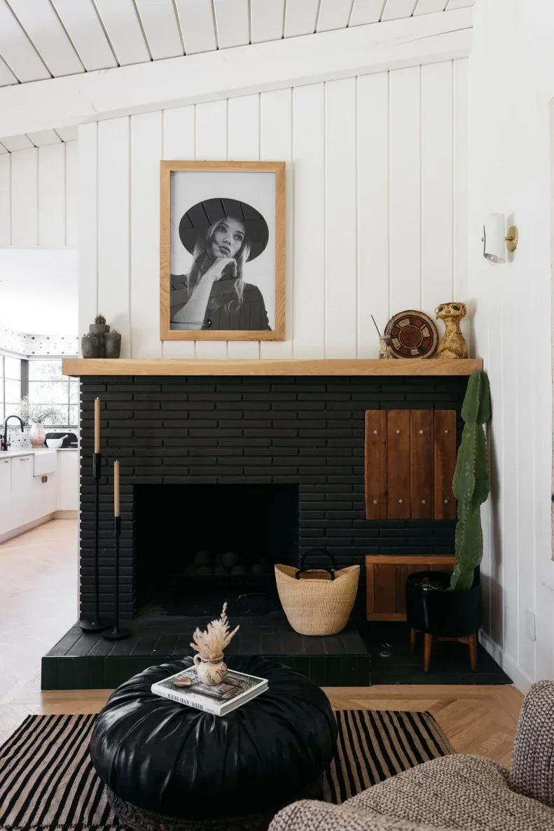 Black brick fireplace with pale wood mantel, framed black and white portrait and small decorative objects