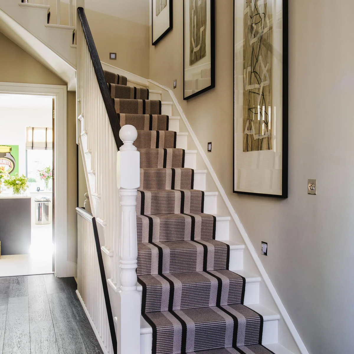 Narrow white staircase with a dark handrail and a beige runner containing strong lengthwise stripes
