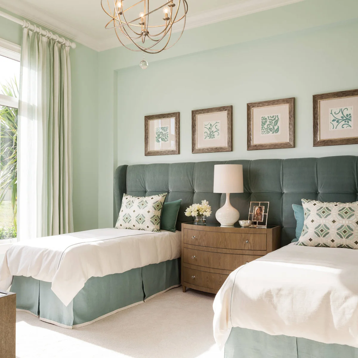 Two beds with pale bedding and green skirts in front of a continuous green upholstered headboard