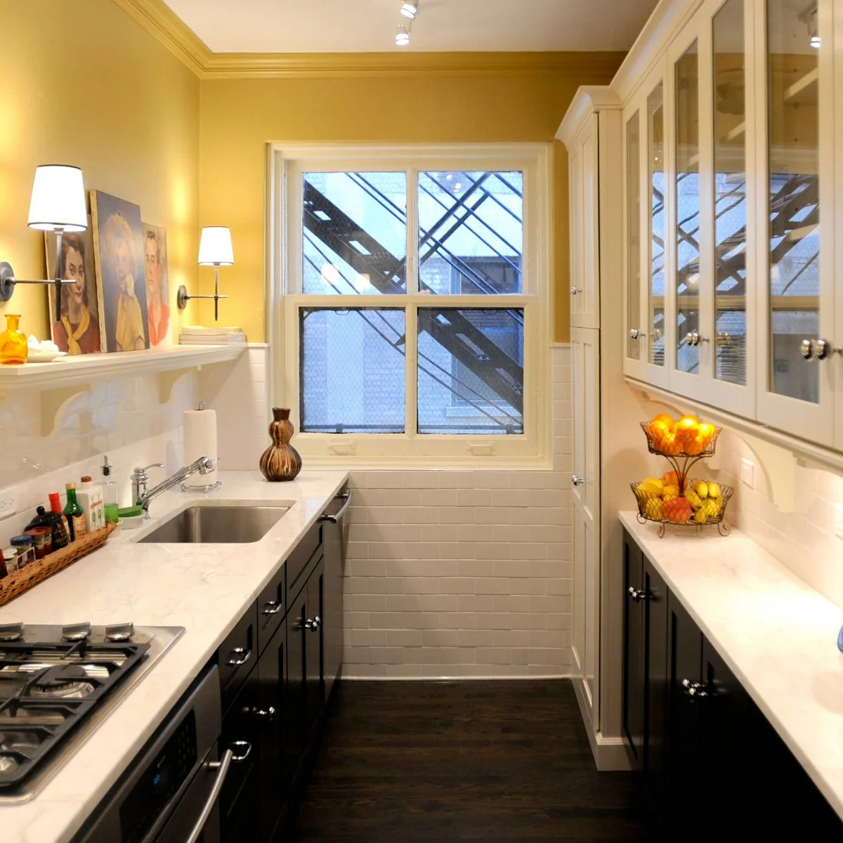 Narrow kitchen with yellow upper walls, white backsplash and dark lower cabinets