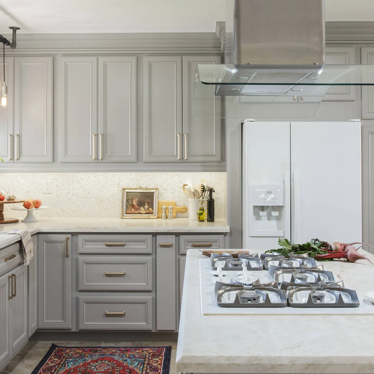 Island cooktop beneath a suspended hood in a gray and white kitchen