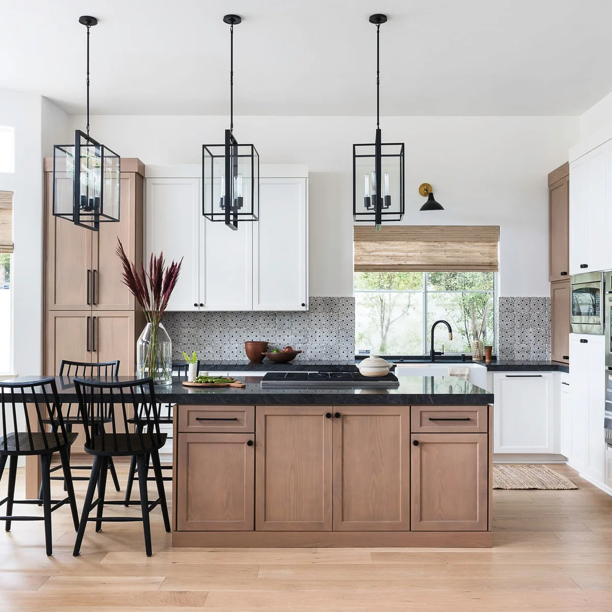 Pale wood and white cabinets surround black counters, dark lantern pendants and dark stools above a light wood floor.