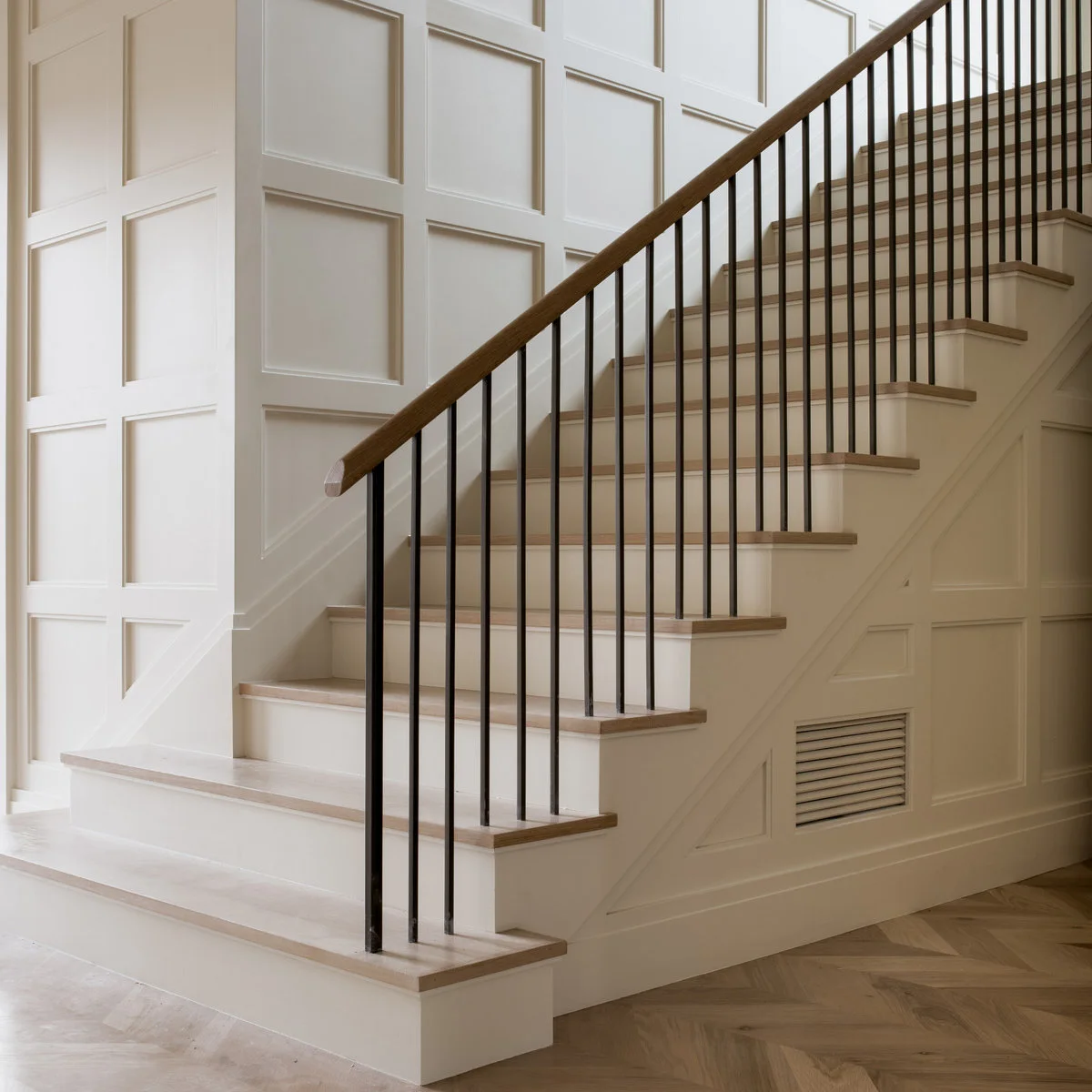 Light wall molding forms rectangular and triangular panels beside pale wood stairs and black balusters.