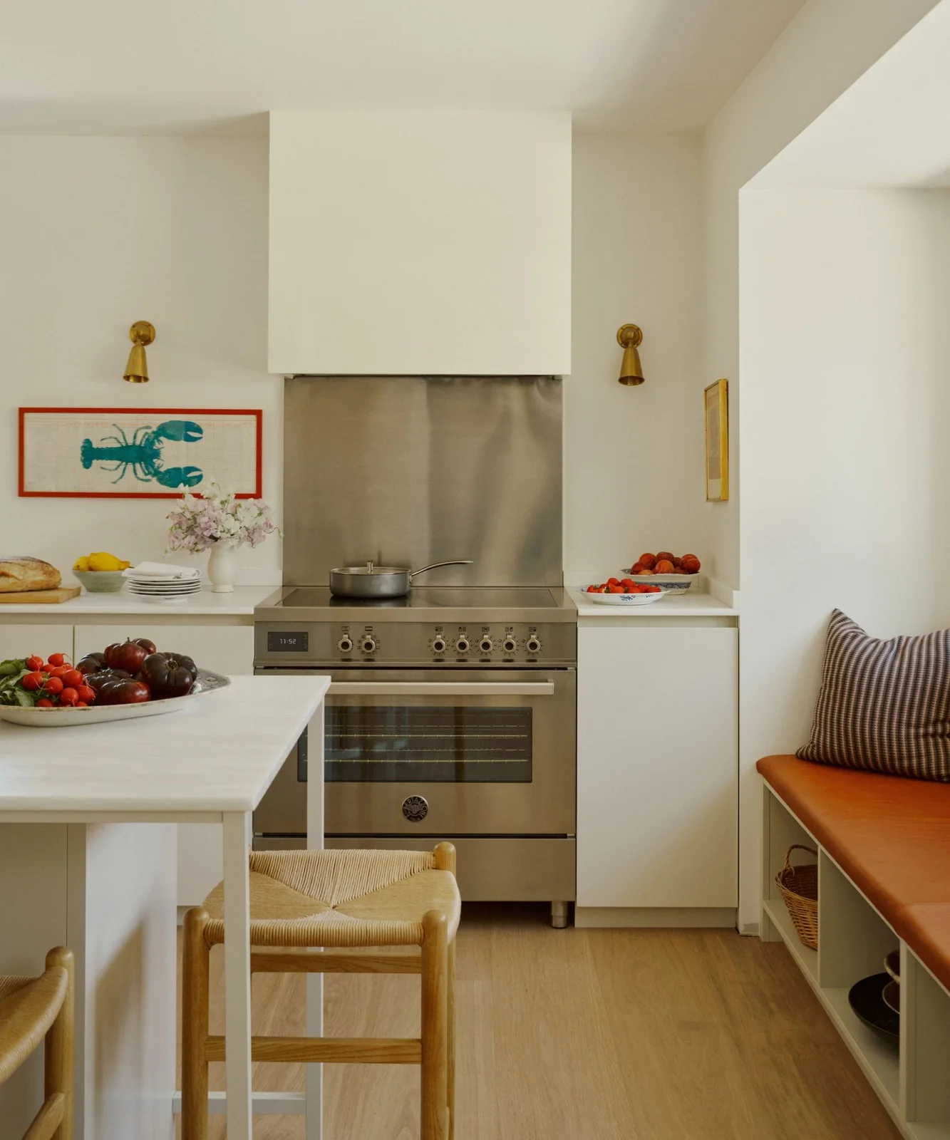 Warm white flat cabinet fronts flank a stainless steel range beneath a broad white hood, with framed red artwork nearby.