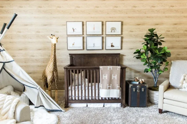 Dark wooden crib beneath small animal-picture group against pale textured wall with decorative giraffe, plant and adult seating.