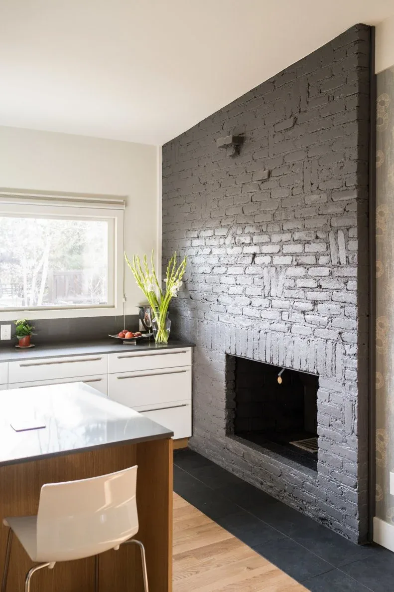Charcoal brick fireplace beside a white kitchen cabinet run and a wooden dining table.
