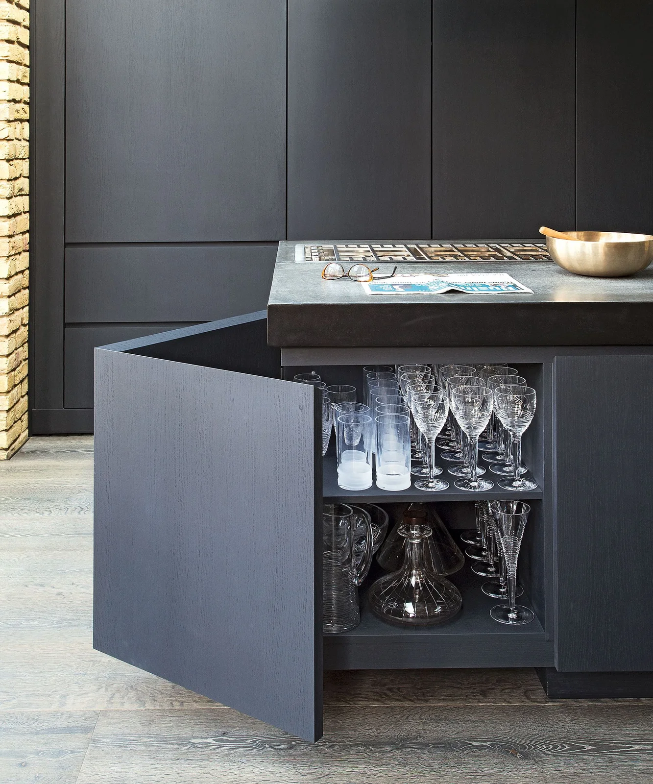 Dark base cabinet with rows of glasses above larger glass serving pieces