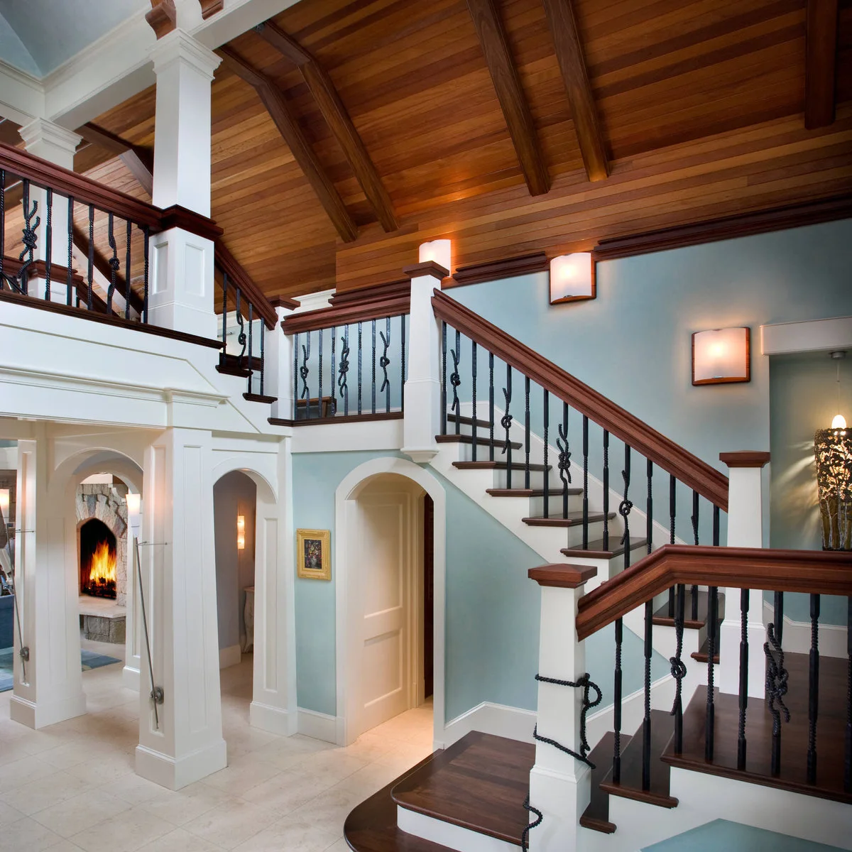 Pale blue stairway walls meet white trim and small square wall lights beneath a wood ceiling.