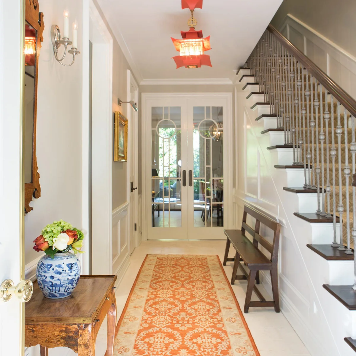 Narrow pale hall with a wooden bench beside the stairs, an orange runner and red hanging lanterns.