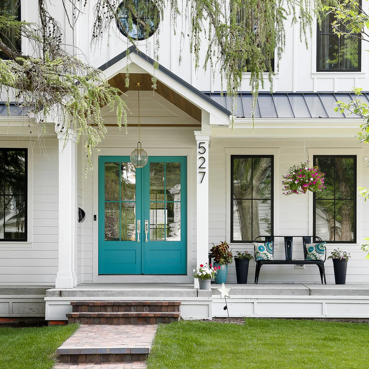 Black porch bench beside turquoise double front doors and a small group of planters