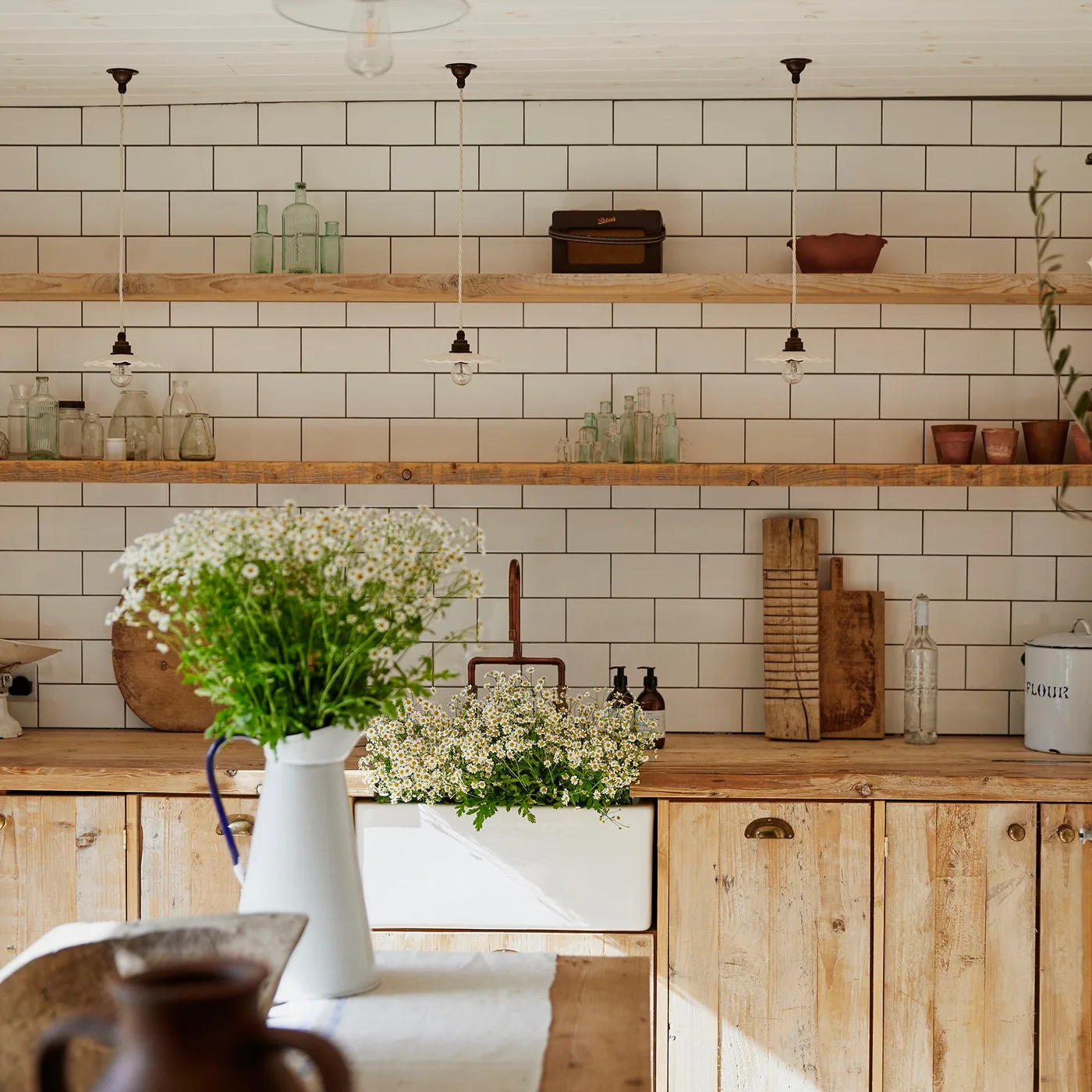 Pale glass bottles and a small radio on two wooden shelves against a white tiled kitchen wall.