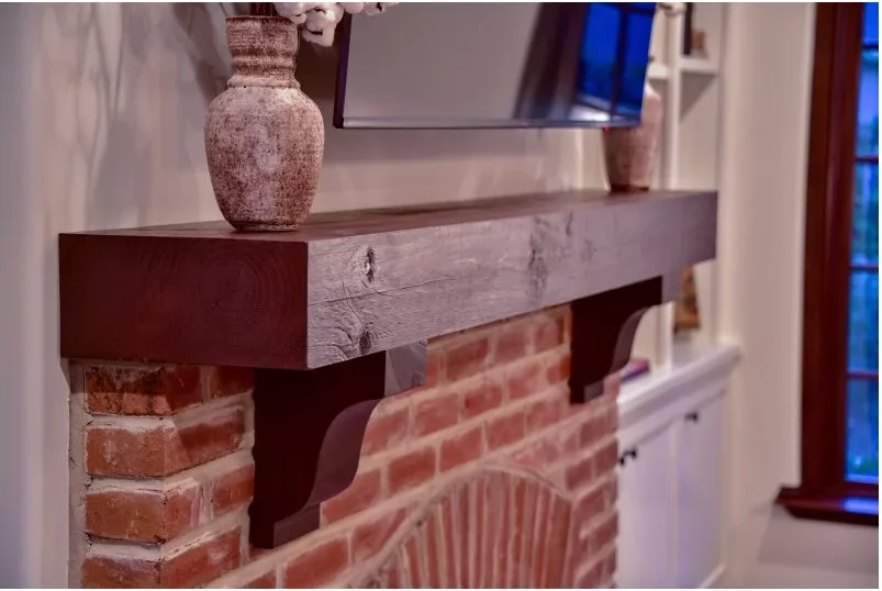 A substantial plain wood mantel shelf rests on shaped corbels above a red brick arched opening beside pale shelving.