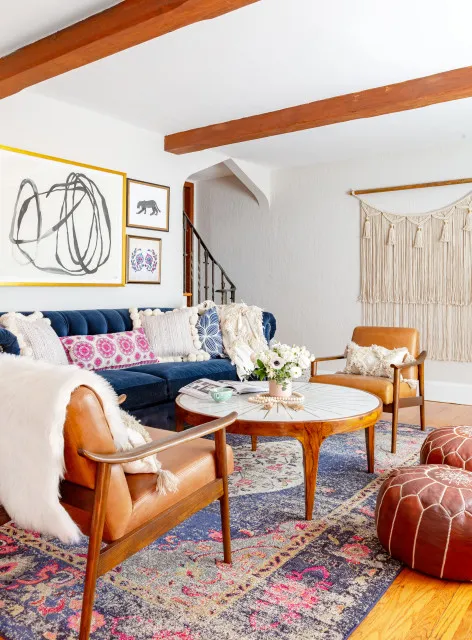 A blue sofa shares a timber-beamed room with tan chairs and a colorful rug.
