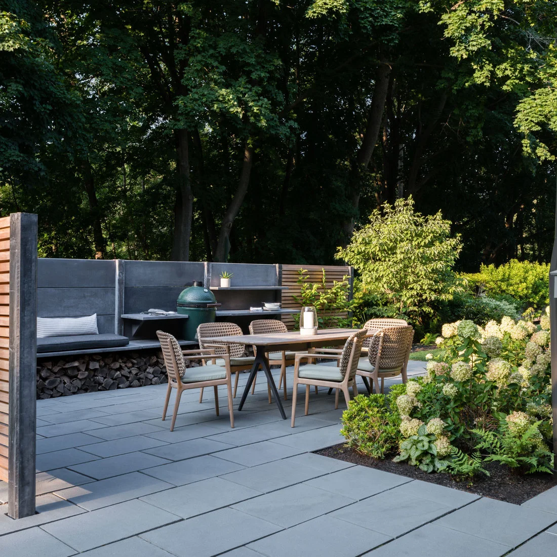 A gray screen stands behind an outdoor dining table beside a grill and low storage