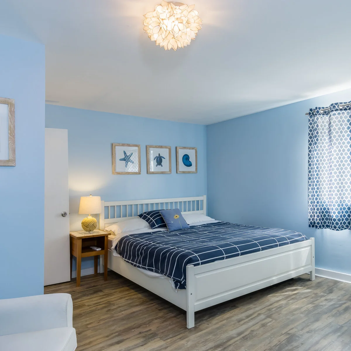 Light blue bedroom walls with sea-life pictures, a white bed and a blue checked duvet.