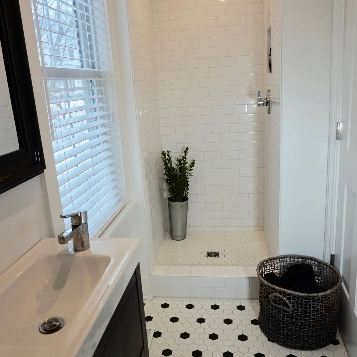 Very narrow bathroom with a small basin, white tiled shower at the far end and black-and-white floor tiles
