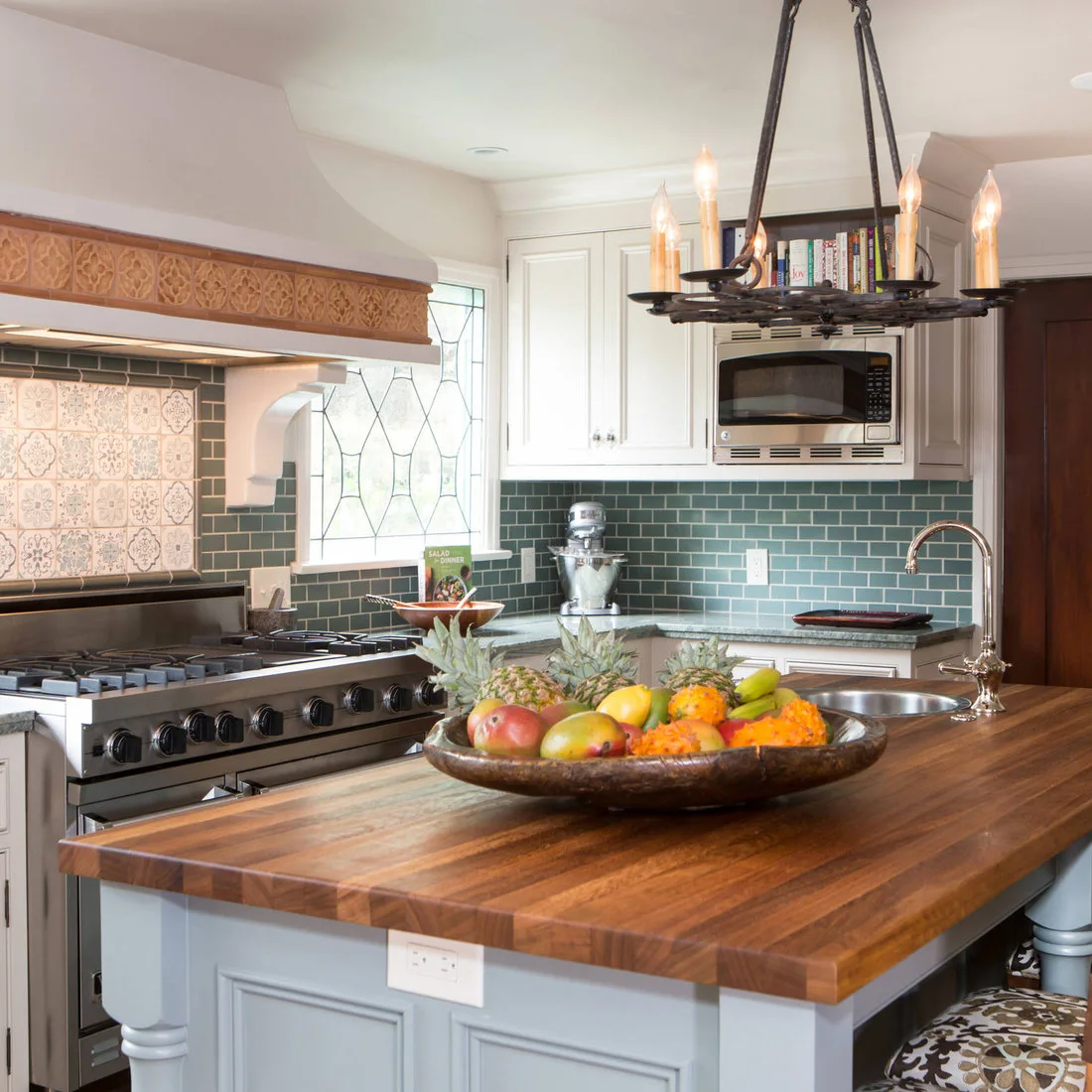 A patterned range panel meets dark green backsplash tiles beside pale cabinets and a timber-topped island.