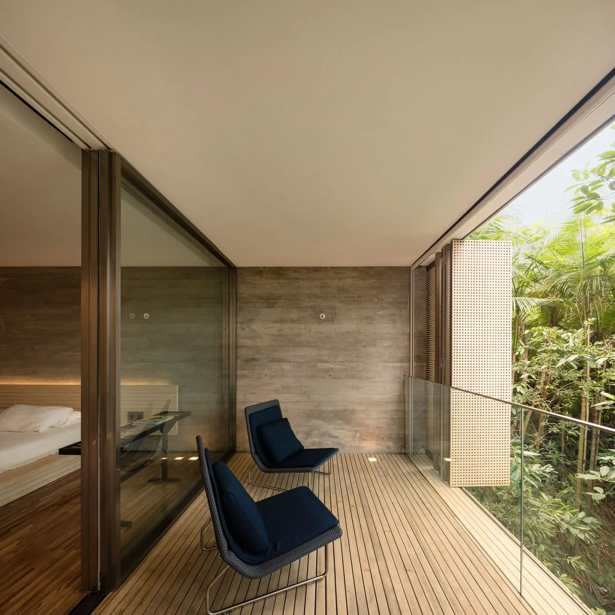 Pale perforated folding panels sit beside a glass railing and dark chairs on a covered balcony