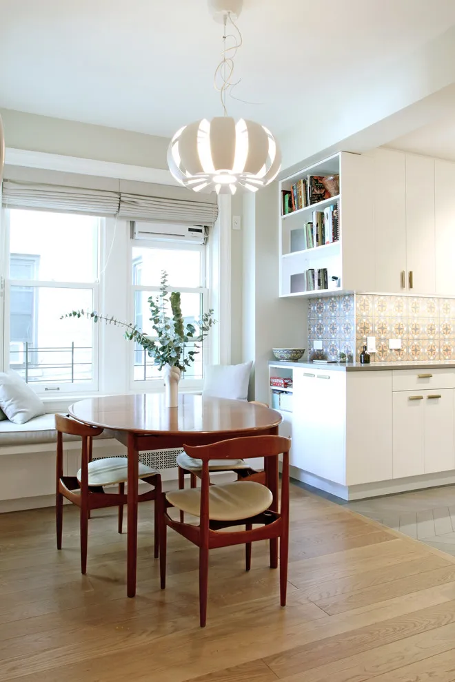 A small round timber table with wooden chairs and pale seat pads stands beside a compact kitchen