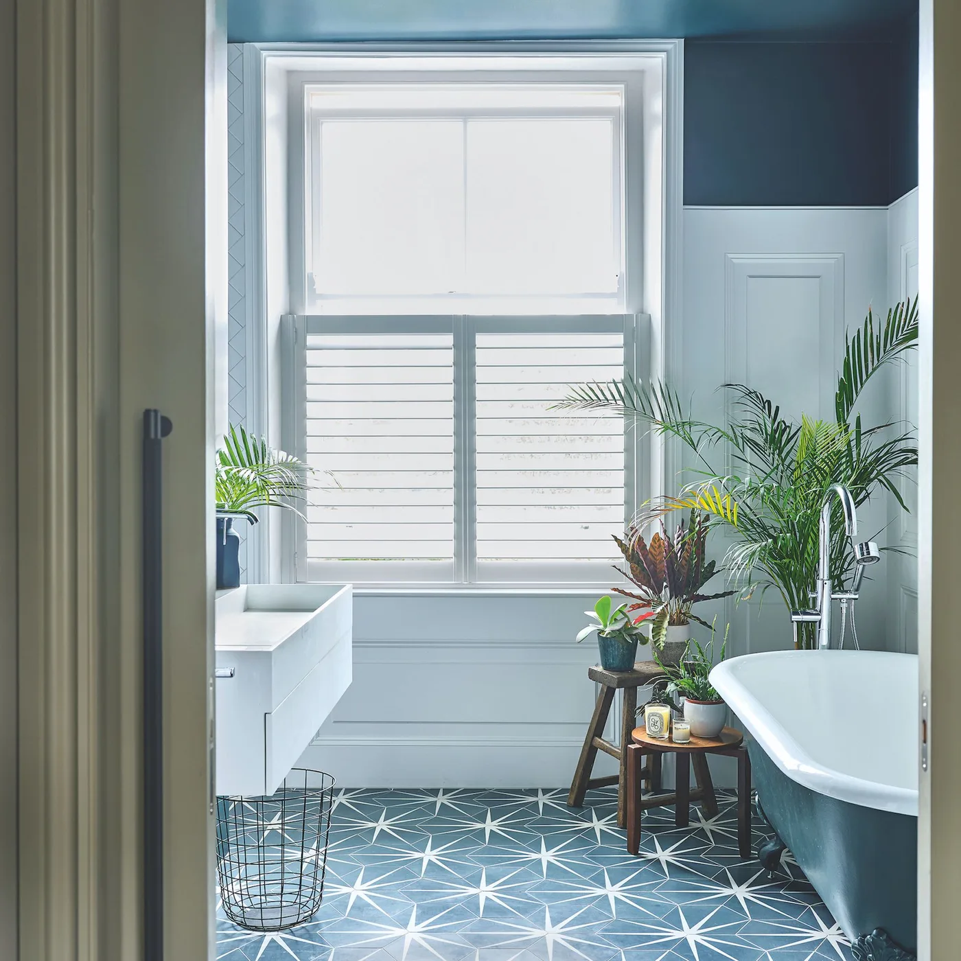 Dark blue upper walls frame a white sash window above pale paneling and a blue patterned floor