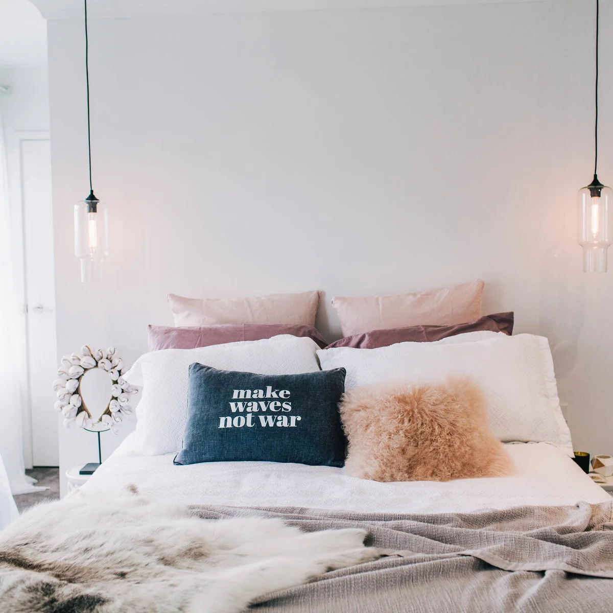 Pale bed with layered cushions, gray throw and small hanging glass lights