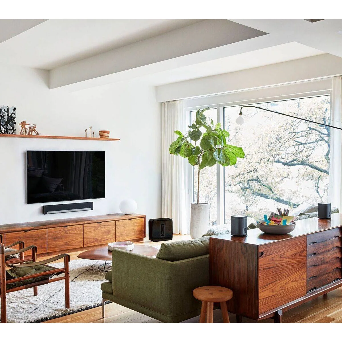 Long wood shelf with a few small sculptures and candlesticks above a wall-mounted television and wood cabinet.