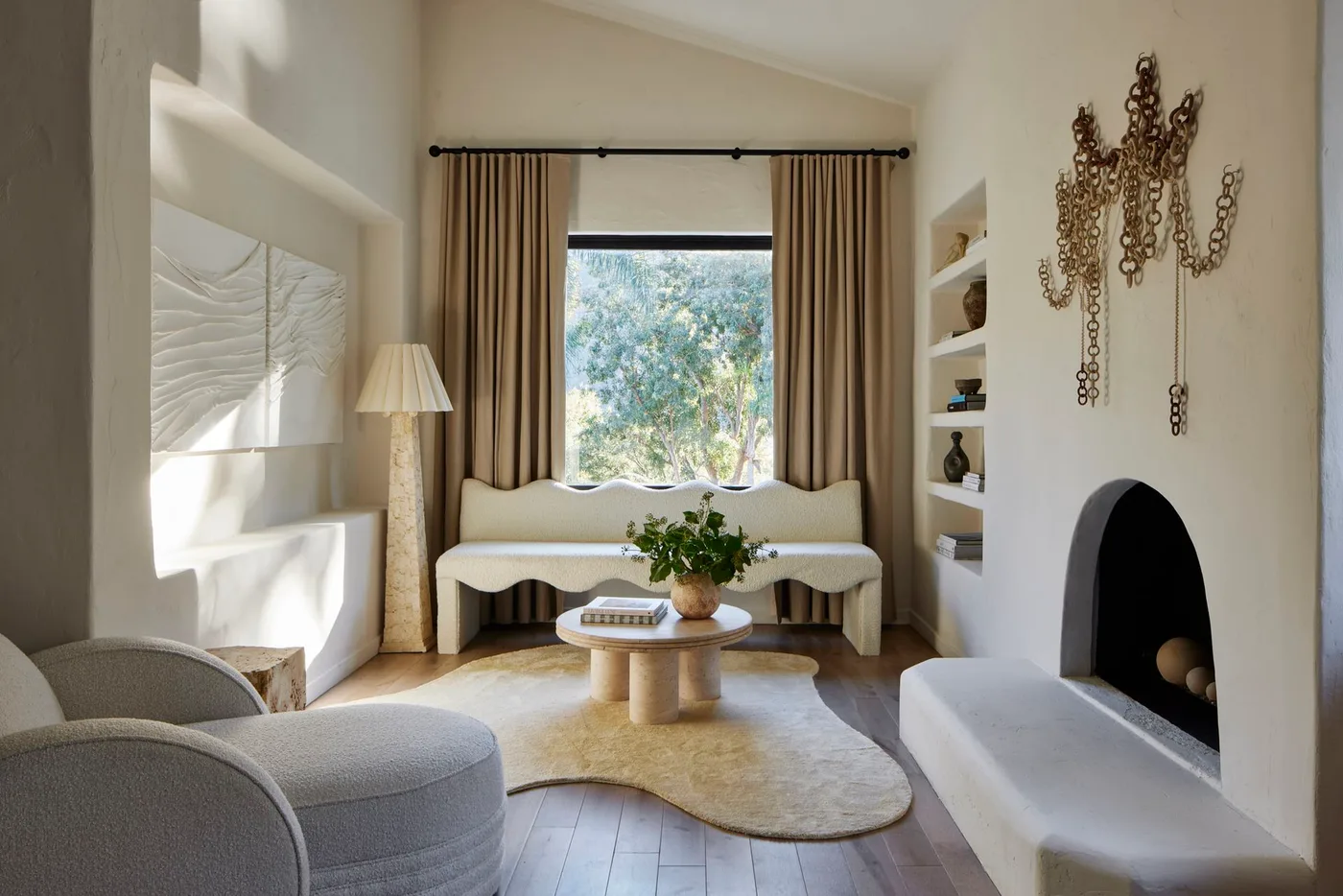 Pale room with arched fireplace, chain-like wall sculpture, curved chair and wavy window bench