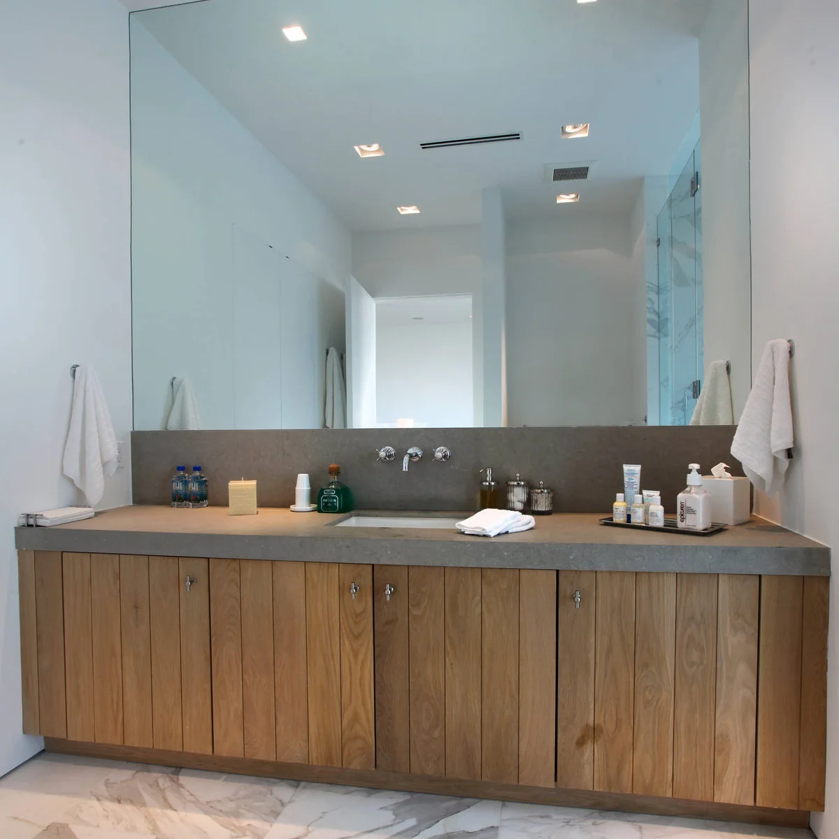 Broad wood vanity with a gray counter, a dark tray of small bottles and tissues, and clear lidded jars.