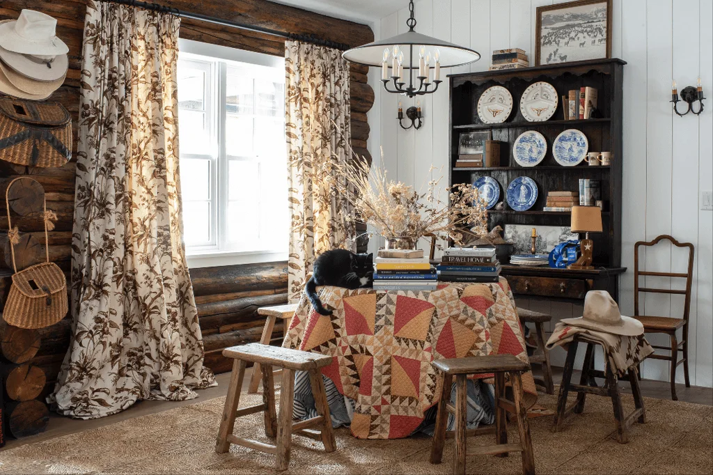 Rustic dining corner with a dark plate dresser, floral curtains, patterned round table and wooden stools