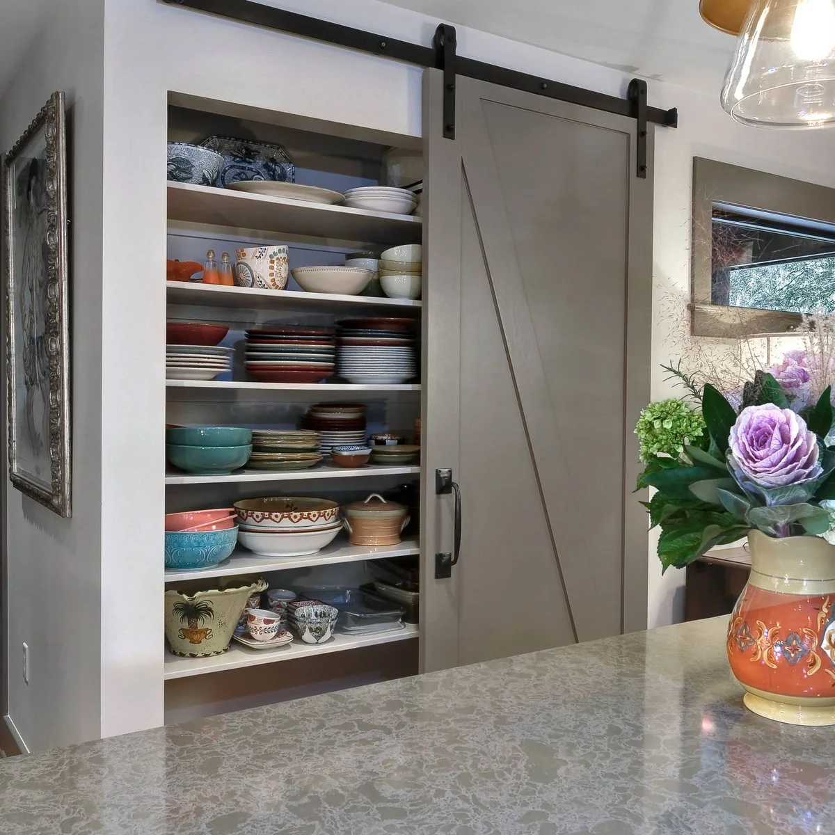 A pale gray sliding door partially covers shallow shelves filled with stacked plates, bowls and serving dishes.