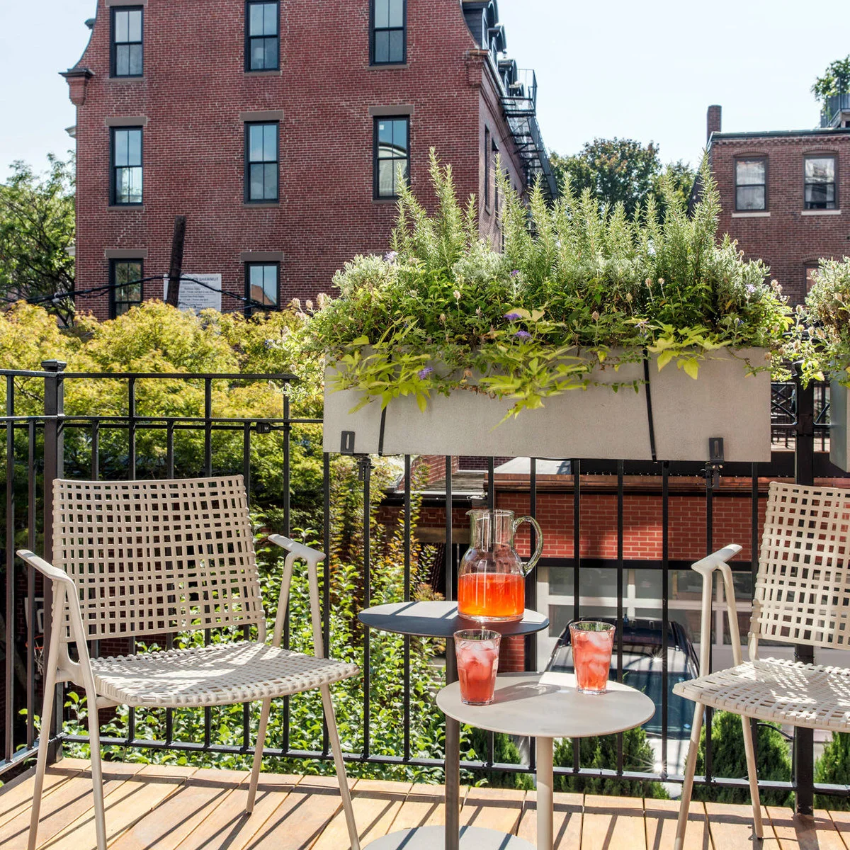 A long railing planter sits behind two light open-backed chairs and small round tables