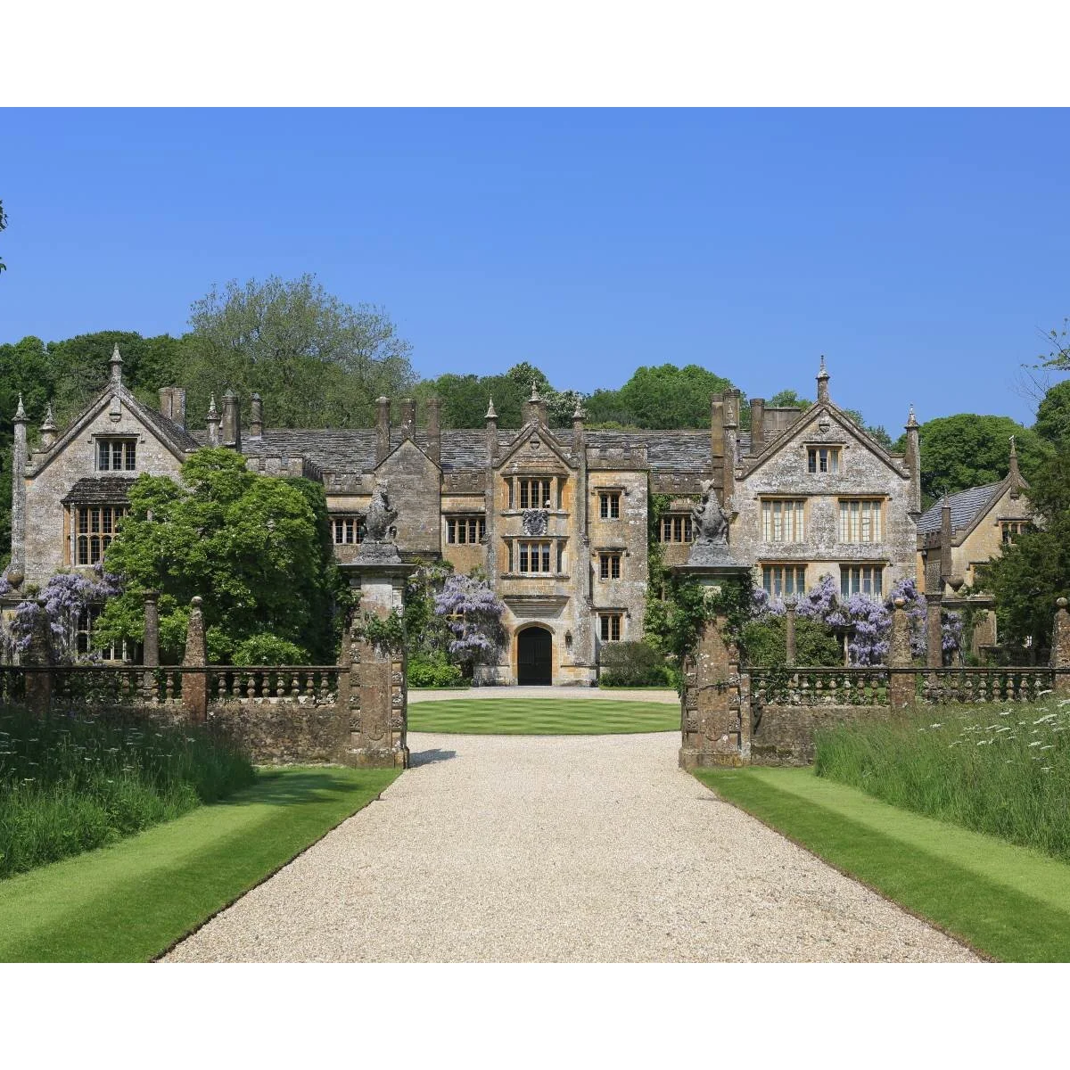 Pale gravel entrance passing through stone gateposts, with short lawn edges and taller meadow-like planting beyond.