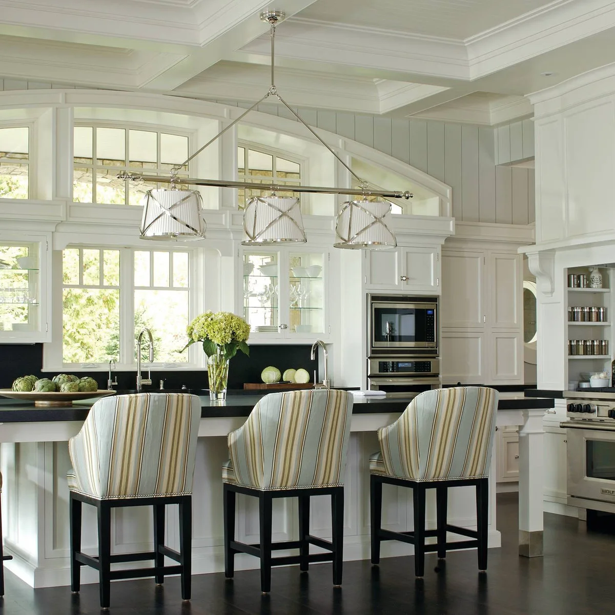 Striped upholstered kitchen stools with short arms, tall backs and dark legs at a raised counter