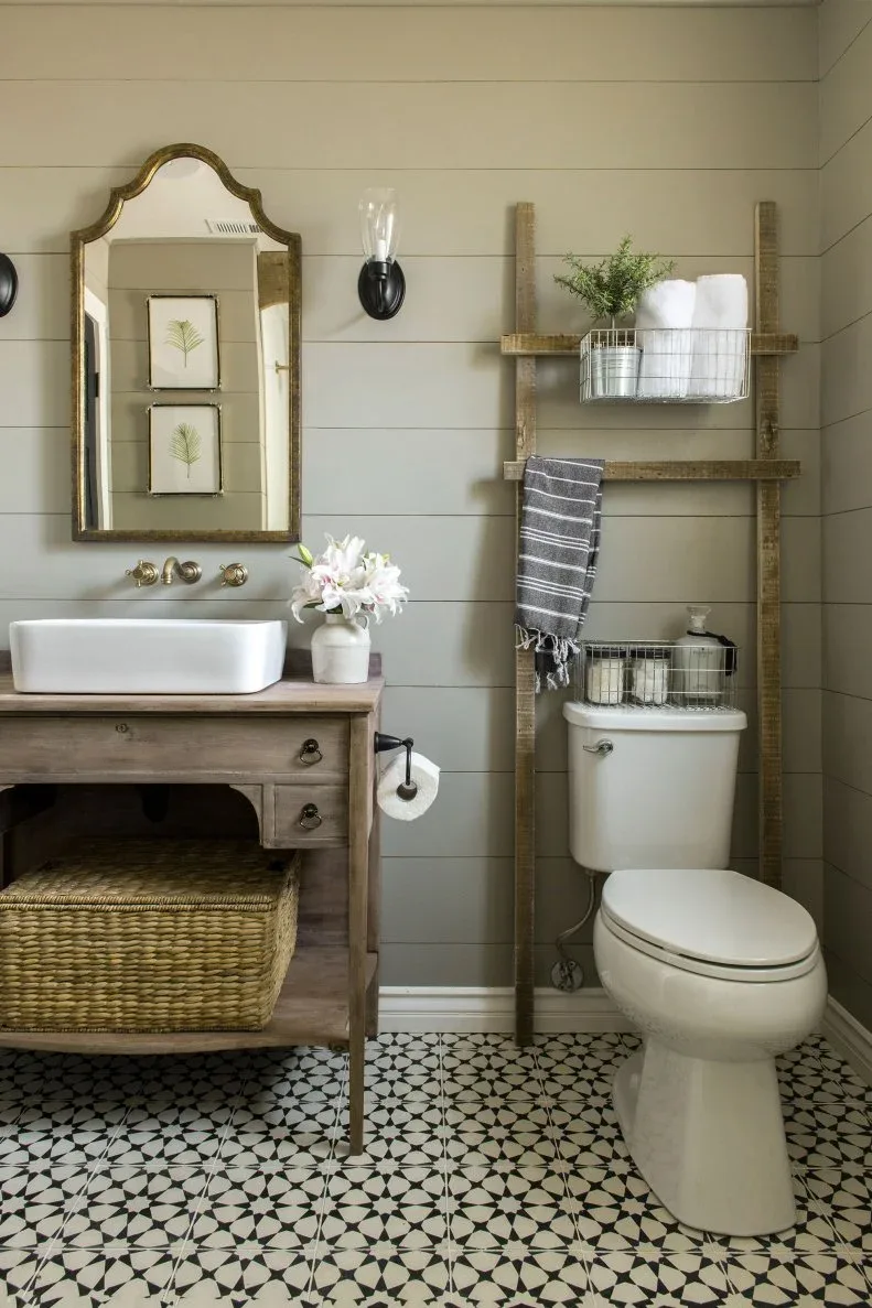 Gray paneled powder room with wood vanity, vessel basin and ladder holding towels and wire baskets