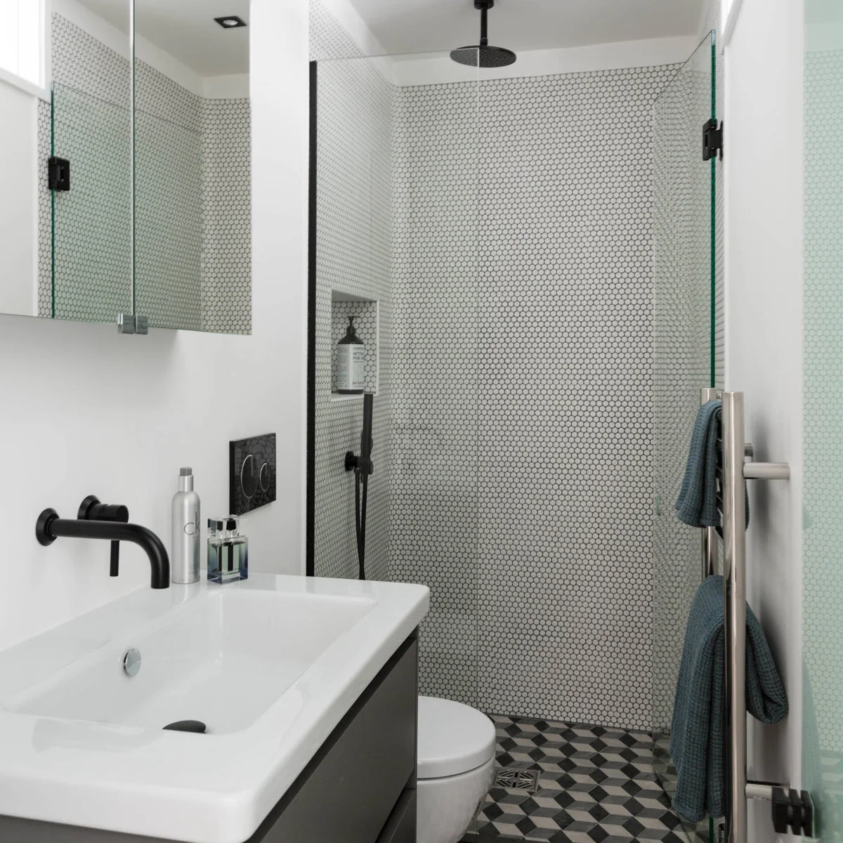 Compact monochrome bathroom with penny-tiled shower walls, black fittings and a geometric floor