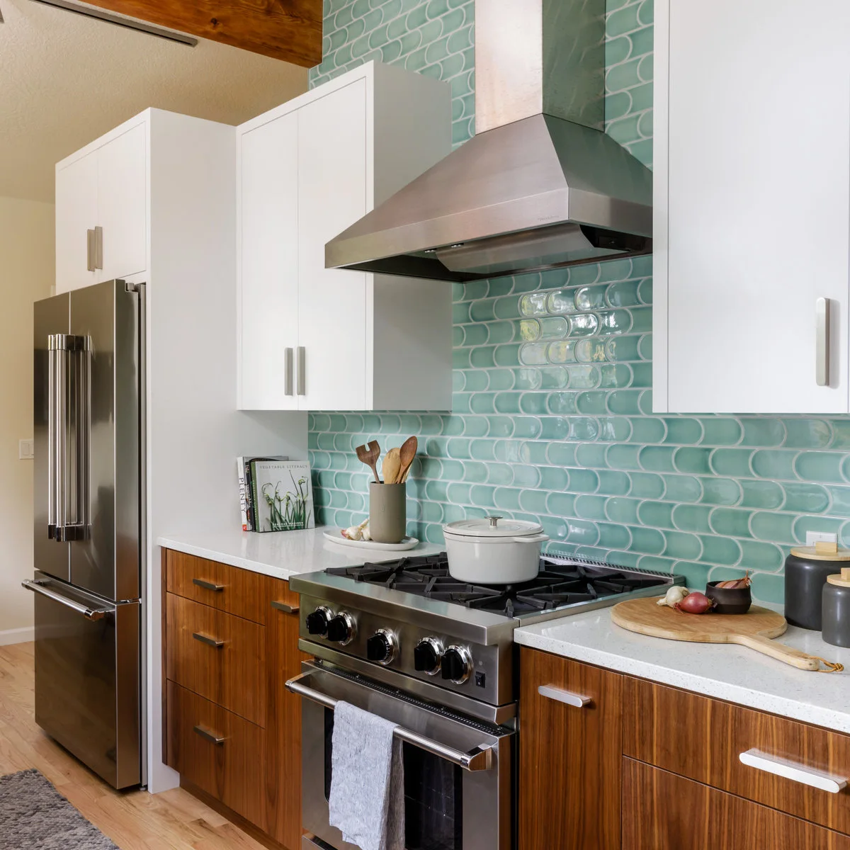Aqua curved rectangular tiles behind a range, with white upper cabinets, wood lower cabinets and a metal hood.
