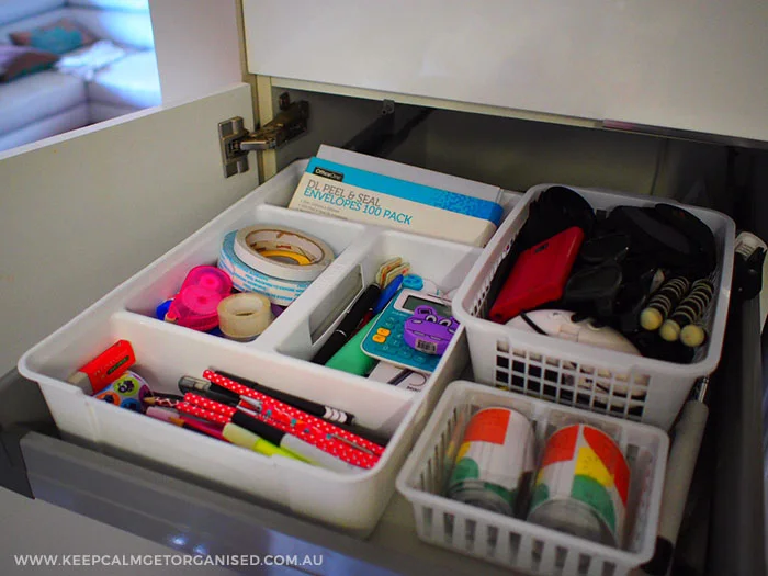 Gray utility drawer with a white divided tray and separate baskets holding household accessories