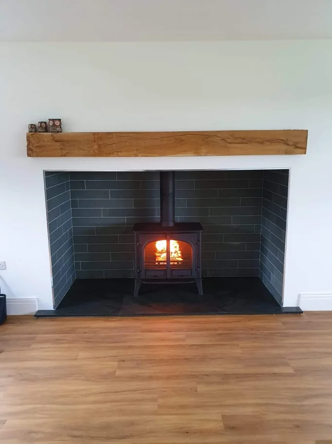 A black stove stands on a projecting slate hearth inside a white chimney breast with a timber mantel.
