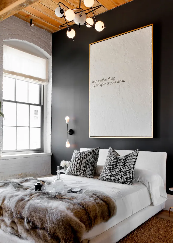 White bedding sits beneath a black wall and a large pale artwork