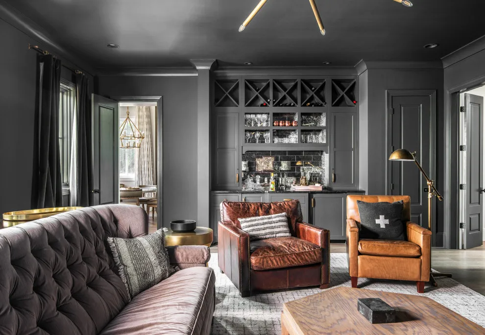 A tufted gray sofa shares a dark room with brown leather and timber-framed chairs