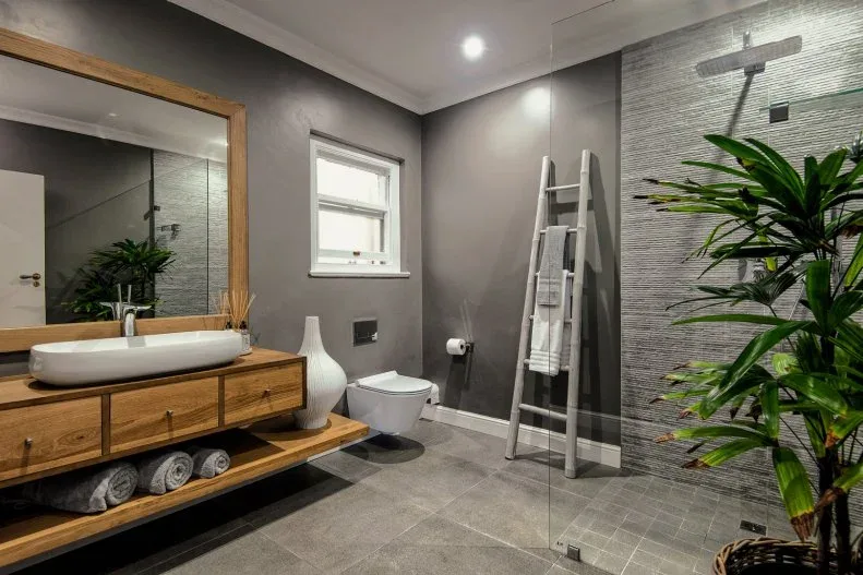 Gray bathroom with a wood vanity, wood-framed mirror, tall leafy plant and pale towel ladder